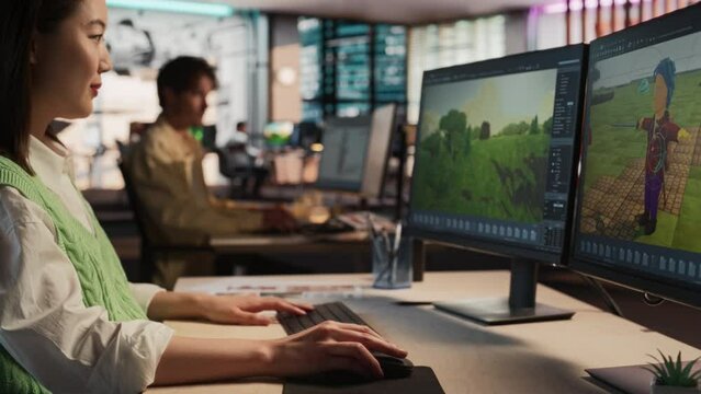 Female Asian Game Developer Using Desktop Computer, Designing Unique World And Characters In 3D modelling Software For Survival Video Game. Creative Woman Working In Diverse Game Design Studio Office.