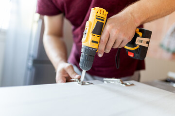 Close up of man assembling furniture by using cordless screwdriver in the kitchen - obrazy, fototapety, plakaty