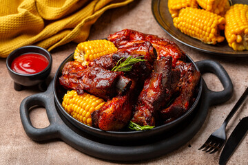 Food board with baked pork ribs with corn cobs, barbecue sauce, rosemary. Brown table background....
