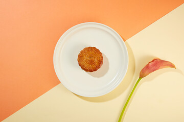 Minimal scene of a baked mooncake placed on white dish decorated with a branch of flower....