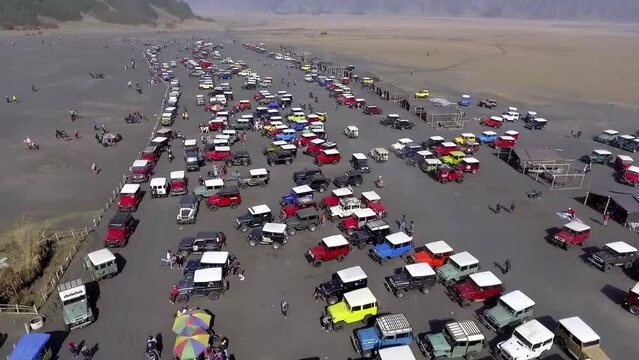 aerial view of hundreds of jeeps parked on a large sandy area at a tourist spot, in the morning, bromo, east java, indonesia