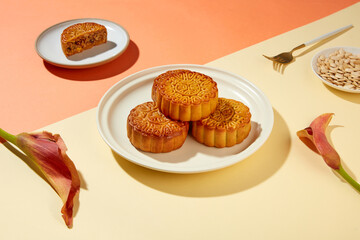 Some traditional mooncakes stacked on each others on white plate. A dish containing pumpkin seeds displayed with a fork and a half of mooncake. Traditions of the Mid-Autumn Festival