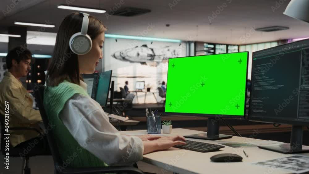 Poster Female Asian Game Programmer Coding On Desktop Computer With Green Screen Chromakey On Display In Game Design Studio Office. Focused Woman Does Gameplay Engineering For New Immersive 3D RPG Video Game
