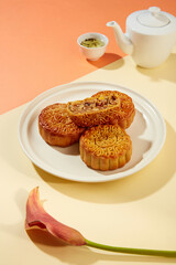 Few baked mooncakes placed on a white plate with a half of mooncake. A tea set decorated with a flower branch. Mid-Autumn Festival is a major holiday in Korea and China