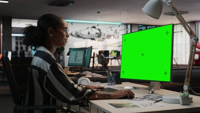 Portrait of Creative Black Woman Sitting at Her Desk Using Desktop Computer with Mock-up Green Screen Chromakey. Female Level Designer Working in Game Design Startup, Creating Immersive Gameplay.