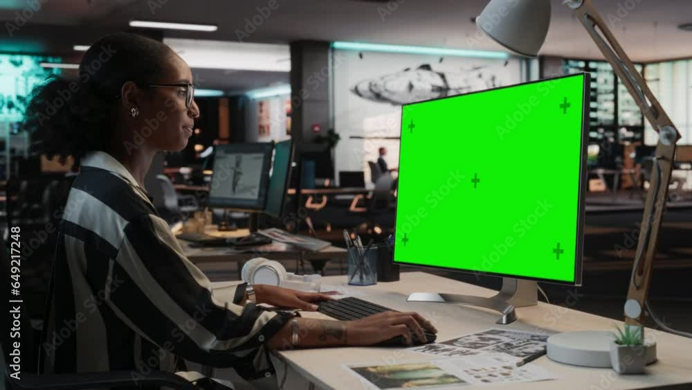 Poster portrait of creative black woman sitting at her desk using desktop computer with mock-up green scree