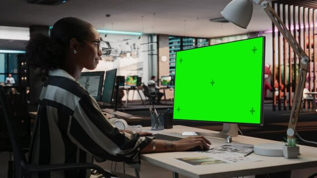 Portrait of Creative Black Woman Sitting at Her Desk Using Desktop Computer with Mock-up Green Screen Chromakey. Female Concept Artist Working in Game Design Startup, Creating Immersive Gameplay.