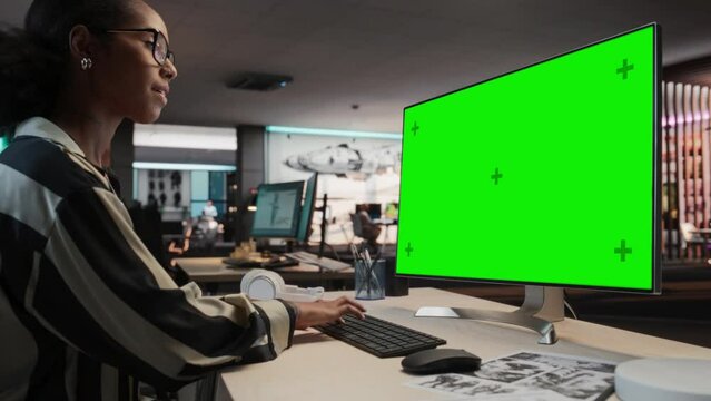 Creative Black Woman Using Desktop Computer with Mock-up Green Screen Chromakey. Female VFX Artist Working in Game Development Company, Creating Immersive Gameplay Elements For Adventure Video Game.