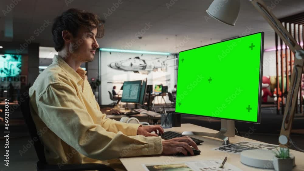 Poster Portrait of Creative Caucasian Man Sitting at a Desk Using Desktop Computer with Mock-up Green Screen Chromakey. Male Concept Artist Working in Game Design Startup Office, Creating Immersive Gameplay.