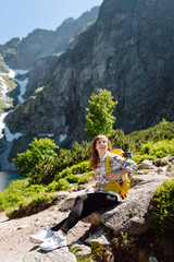 Naklejka na ściany i meble Portrait of a happy female traveler with a yellow hiking backpack standing on the top of a mountain. Concept of nature, sport, adventure.