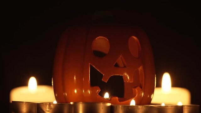 Illuminating pumpkin for Halloween rotating on darkness background with burning wax candles. Pumpkin glows on Halloween night