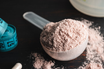 Scoop of chocolate whey protein isolate, white capsules of amino acids, creatine and measuring tape, bodybuilding food supplements on a dark wooden board