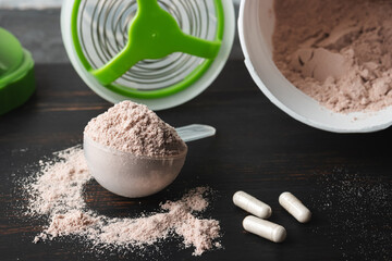 Scoop of chocolate whey protein isolate, white capsules of amino acids and creatine, bodybuilding...