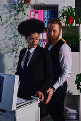 businessman seducing displeased african american woman frowning near copier in night office
