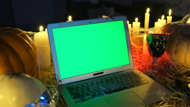 Terribly background Happy Halloween, laptop with green screen and glass of blood, candles, pumpkins, spiders and skulls, a vampire crypt. Advertising scary game and creepy posts on social networks