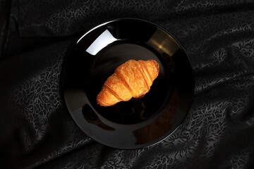 The Croissant on a Black Plate on a Black Fabric Background