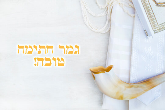 Translation title: May you be signed and sealed in the book of life. in Hebrew. 
A shofar is placed on a tallit and siddur book on a white background. greeting card and Yom Kippur Rosh Hashanah 
