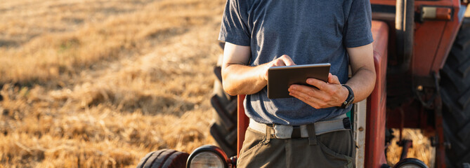 Farmer with a digital tablet is next to an agricultural tractor.