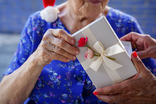 Unrecognizable Old Woman Receiving A Christmas Gift In December. Loneliness In Old Age