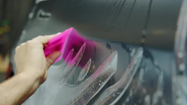Process of applying a protective PPF film to a car. Hands of a professional applying a protective film of laminate. Closeup view