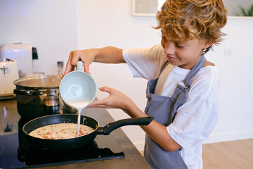 Crop boy pouring milk cream into pan on stove