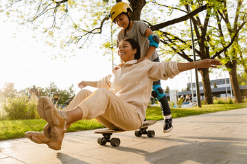 Cheerful boy riding his mother on skateboard in park © Drobot Dean