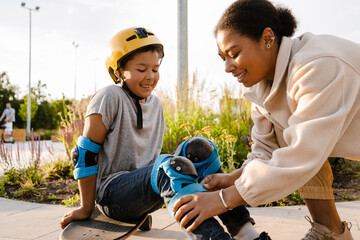 Smiling mother putting safety gear on her son at skatepark