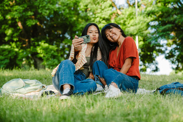 Naklejka na ściany i meble Two asian women taking selfie while sitting in green park