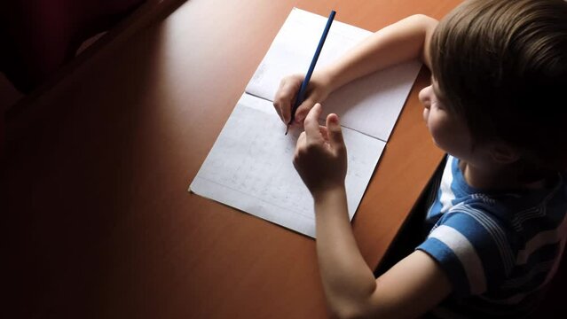 The child writes down the answer to the solution of the example in a copybook. A mathematics homework. A boy diligently learns to write. The kid is sitting at the table and doing a task. Smart person.