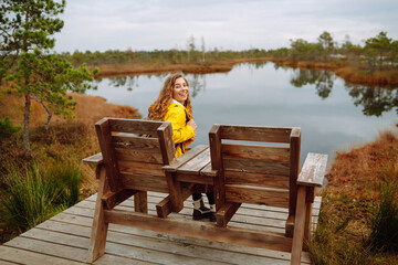 A hiker female wearing a yellow coat and backpack walks along a scenic nature trail with a wooden...