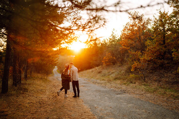 Obraz premium A couple in love in casual clothes are walking, drinking tea from a thermos, enjoying the autumn weather in the forest. Concept of vacation, weekend, love.