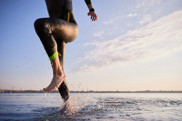 Cropped image of male body, leg in wetsuit running out of river after training in early morning....