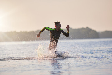 Professional sportsman in wetsuit running into water, swimming, training in morning. Speed and...