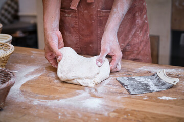 Male baker's hands working bread dough with flour on a wooden ta