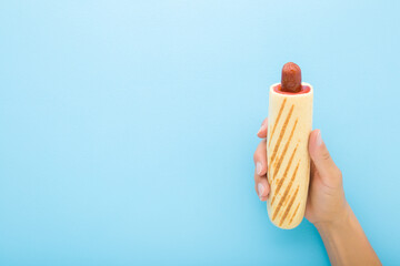 Young adult woman hand holding fresh french hot dog with red ketchup on light blue table background. Pastel color. Closeup. Fast food. Empty place for text. Top down view. - obrazy, fototapety, plakaty