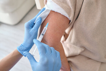 Crop nurse in sterile gloves vaccinating patient with syringe