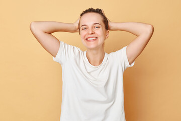 Healthy hair. Wellbeing wash. Pampering routine. Satisfied smiling woman wearing white T-shirt washes hair standing with shampoo foam on her head isolated over beige background