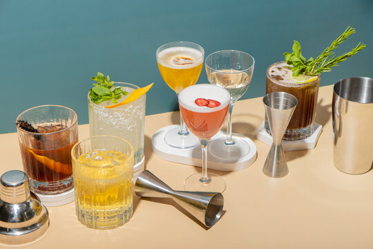 Bar tools and alcoholic cocktails on podiums on colored background. Signature cocktails concept