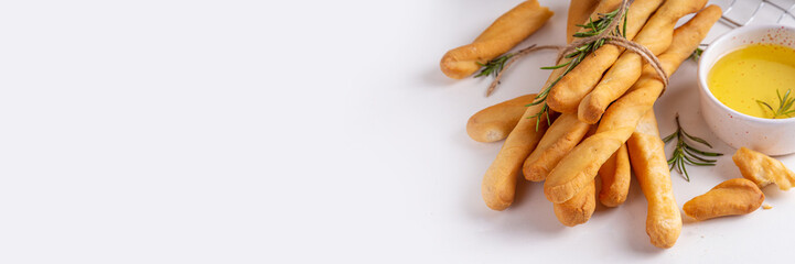Italian Mediterranean grissini bread sticks, with aromatic oil and sprigs of rosemary, on a white kitchen table background