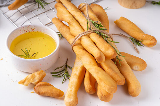 Italian Mediterranean grissini bread sticks, with aromatic oil and sprigs of rosemary, on a white kitchen table background