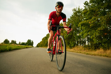 Naklejka premium Dynamic image of motivated sportsman, athlete riding bicycle along the road, training outdoors. Concept of professional sport, triathlon preparation, competition, athleticism
