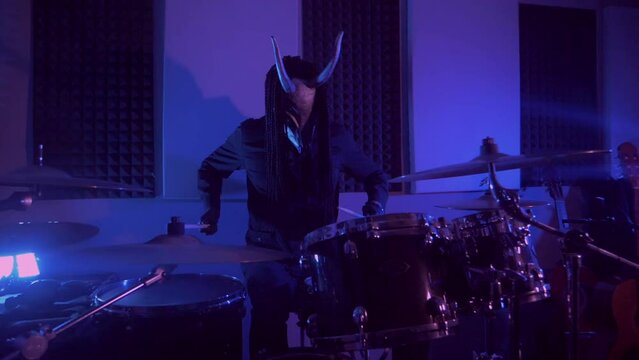 The devil monster plays the drums. A mystical man in a scary mask in a dark studio. Horror, Halloween