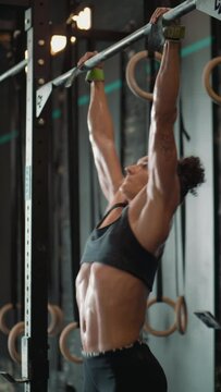 Vertical shot of a focused woman  doing pull-ups on the bar, training at a gym