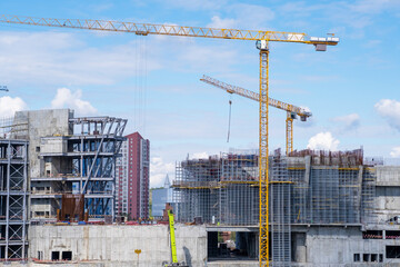 A crane and a building under construction against a blue sky background. Builders work on large...