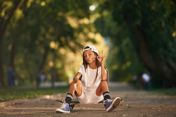 Chilling, sitting and relaxing. Happy little girl with skateboard outdoors