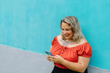 Smiling woman with smartphone on blue wall