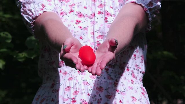 Close-up of a girl's hands in a delicate white summer dress. She opens palms, which contain a red butt plug. Sex toys, Sex shop. BDSM - outfit for adult sex games
