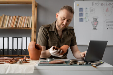 Archaeological digging. Male archaeologist doing research, using laptop computer, analysing ancient...