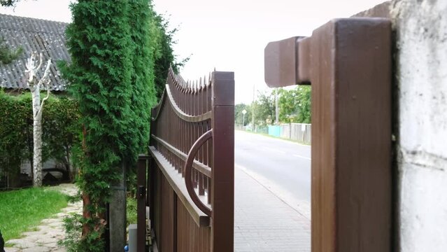 Closing of automatic entrance gate of brown color made of metal. Block fence. Entrance group for cars in the private house. Distance control. Smart home system. Close-up.