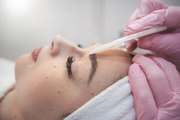 cosmetologist doing medical procedure with white gouache scraper on a client's face
